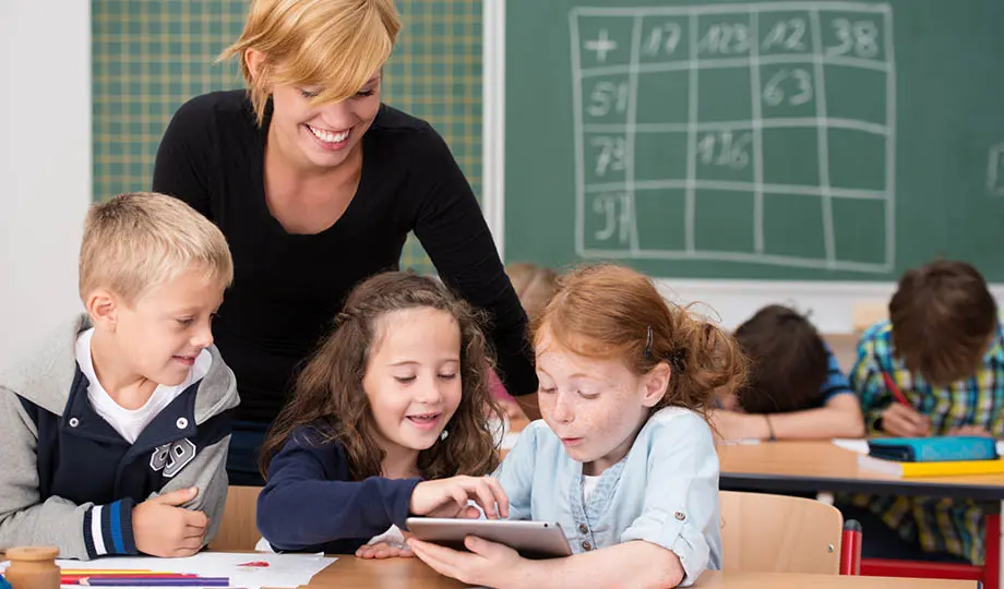 Kvinnlig pedagog i klassrum med tre små elever i förgrunden och tre i bakgrunden