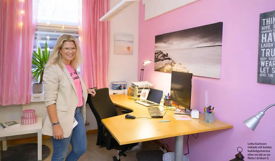 kvinna står vid skrivbord i kontorsrum med rosamålad vägg